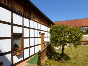 Fachwerkscheune mit Holzgeländer und Bäumchen im Garten
